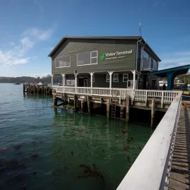 View of the Stewart Island Visitor Terminal, with a wooden pier extending into the calm harbor waters.