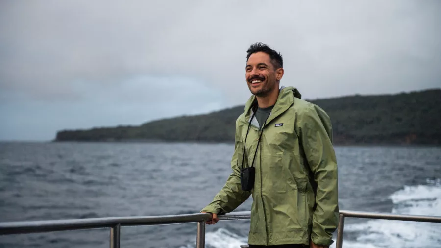 A smiling passenger aboard the Stewart Island ferry on a scenic journey, with coastal views in the background.