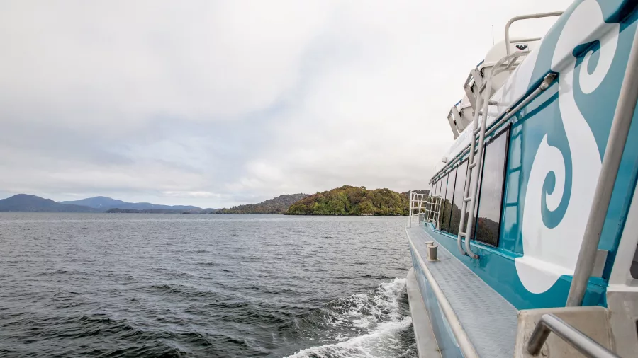 The side view of a ferry traveling towards Stewart Island with lush green hills visible in the background.