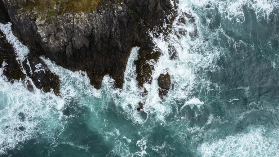 Aerial view of waves crashing against the rugged coastal cliffs of Stewart Island.