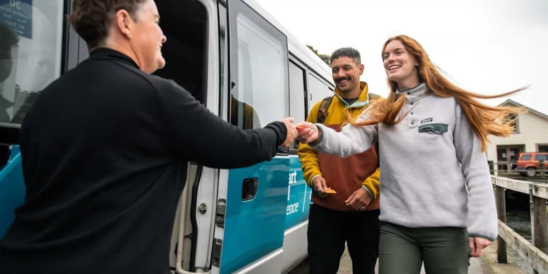 Smiling visitors receiving a warm welcome before boarding the Stewart Island Experience bus.
