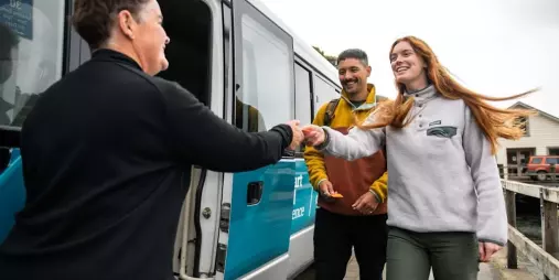 Smiling visitors receiving a warm welcome before boarding the Stewart Island Experience bus.
