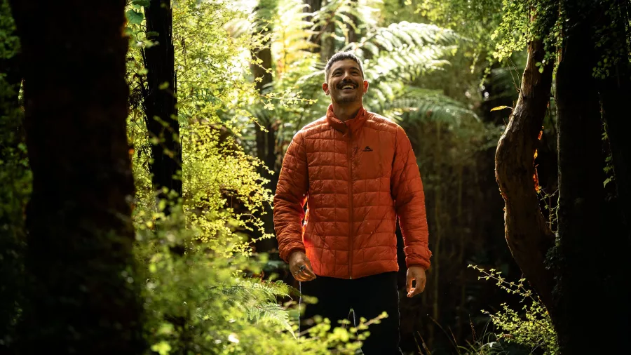 Walker smiling while exploring sun-dappled native forest at Oneke on Stewart Island