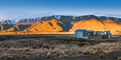 Sunrise lighting up mountains behind an abandoned hut in the Maniototo region