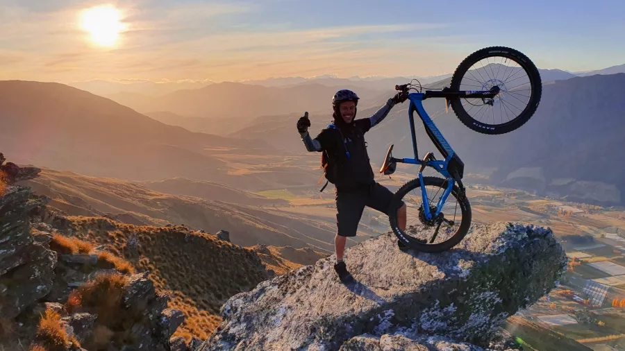 Rider lifting e-bike on a rock at sunset with mountains in the background