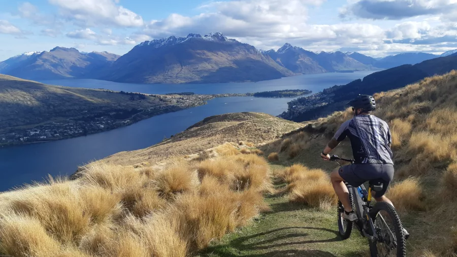E-biker descends a mountain trail with Lake Whakatipu and Queenstown below