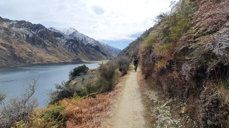 Rider cruising along the scenic Kawarau River trail with snowy peaks in the background