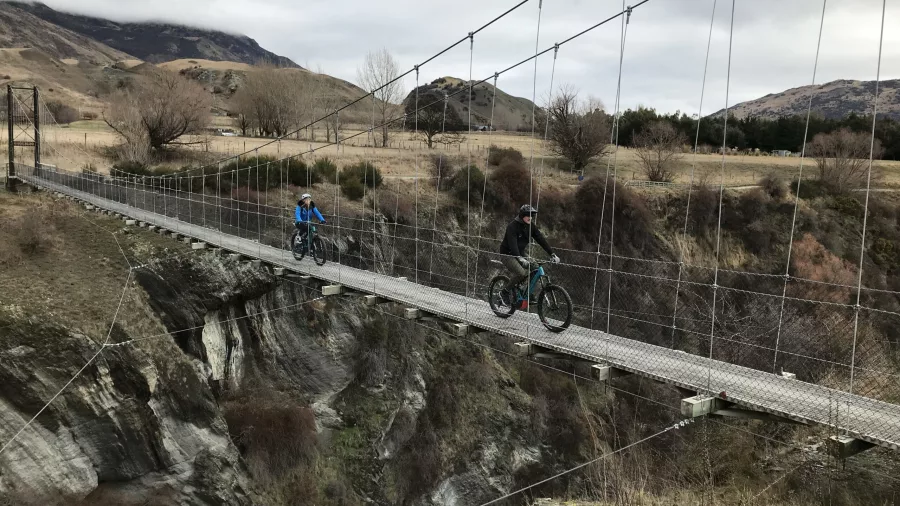E-bikers crossing a swing bridge over a gorge in Gibbston Valley