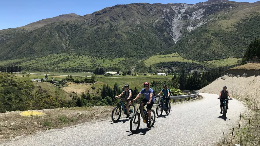 Group riding e-bikes on open road with mountains in Gibbston Valley