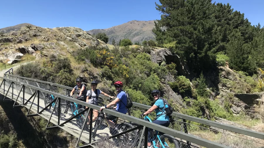 Group of cyclists crossing bridge on e-bike wine tour in Gibbston Valley