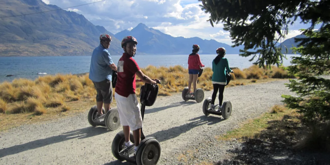 Segway group riding along a gravel track with Lake Whakatipu and mountains in view