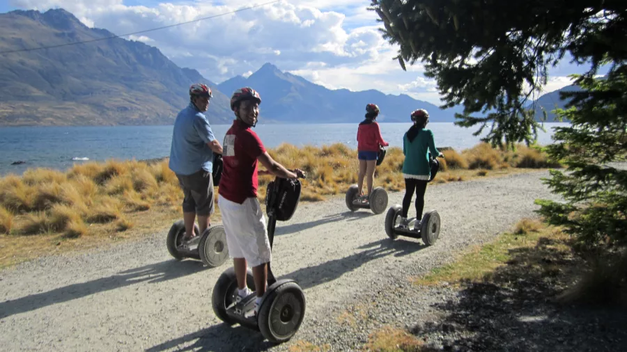 Segway group riding along a gravel track with Lake Whakatipu and mountains in view