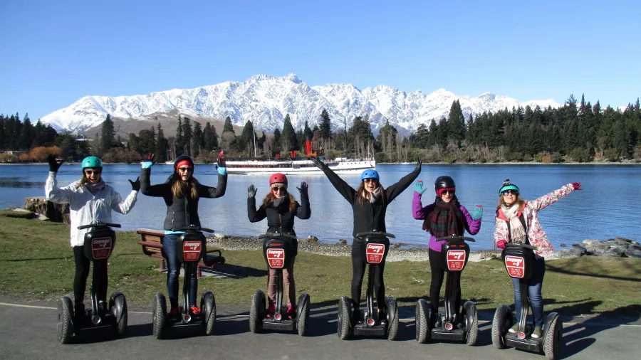Happy Segway riders with snow-covered Remarkables and Lake Whakatipu in the background