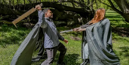 Two guests in cloaks staging a sword duel in a forest setting during a LOTR tour