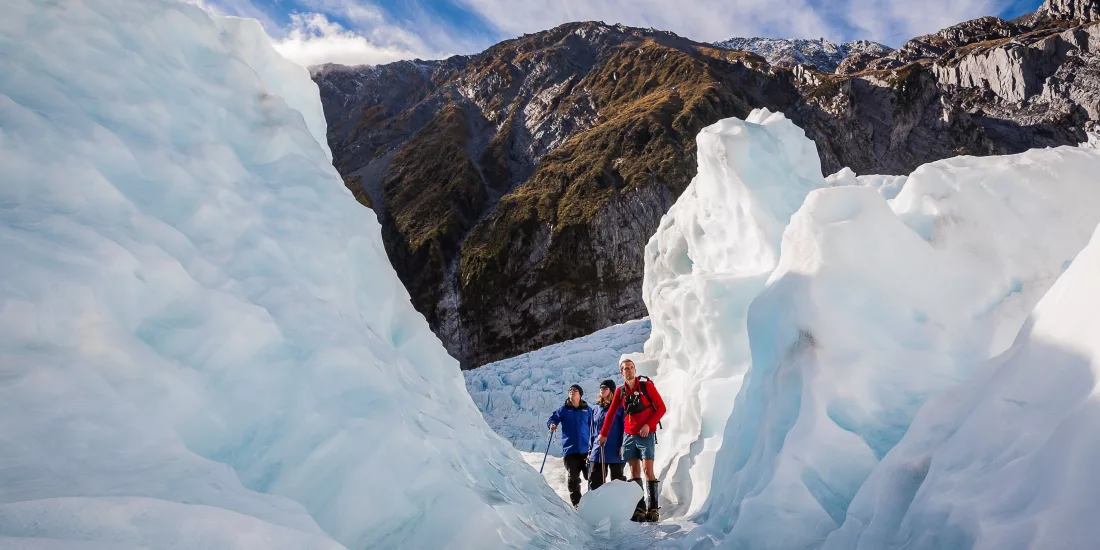 Three hikers walking through towering ice walls on a guided glacier hike at Franz Josef