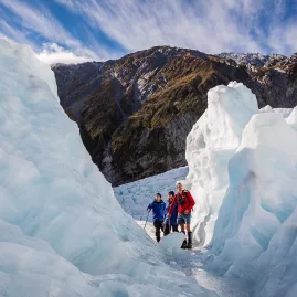 Three hikers walking through towering ice walls on a guided glacier hike at Franz Josef