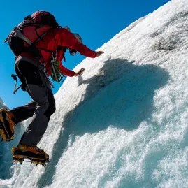 Climber using crampons to scale an icy slope on a glacier tour at Franz Josef
