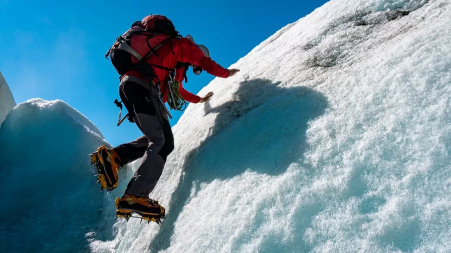 Climber using crampons to scale an icy slope on a glacier tour at Franz Josef