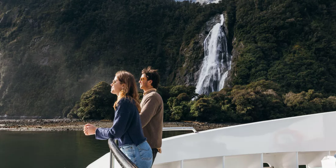 Couple on the bow of a Pure Milford cruise boat viewing Bowen Falls in Milford Sound