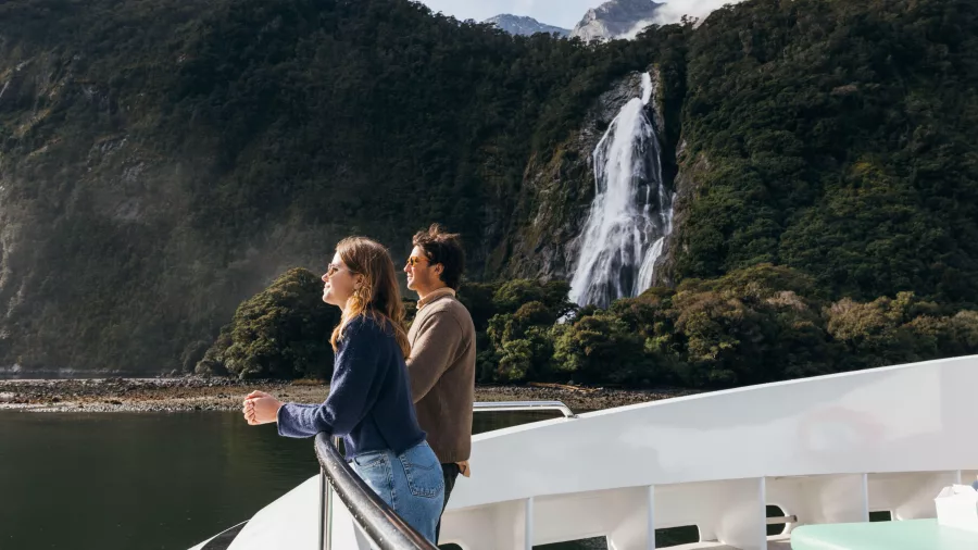 Couple on the bow of a Pure Milford cruise boat viewing Bowen Falls in Milford Sound