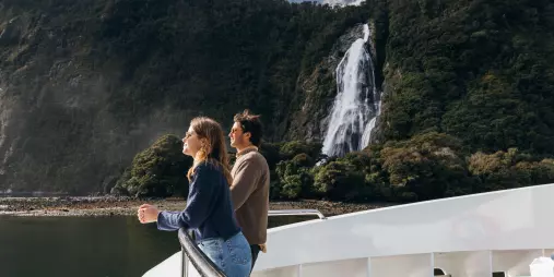 Couple on the bow of a Pure Milford cruise boat viewing Bowen Falls in Milford Sound
