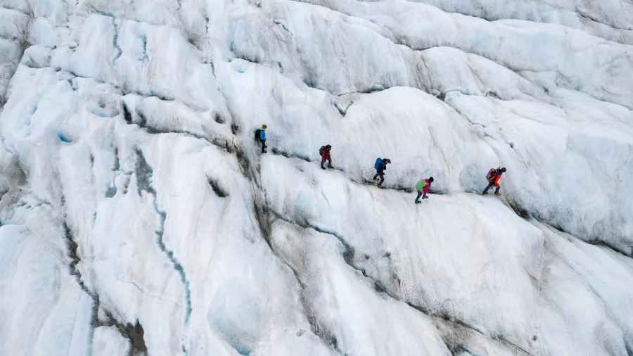 Aerial view of hikers carefully climbing icy ridgelines on the Tasman Glacier