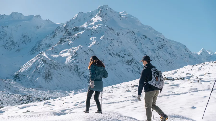 Couple walking in snow near Mount Cook with glacier-covered peaks in the background