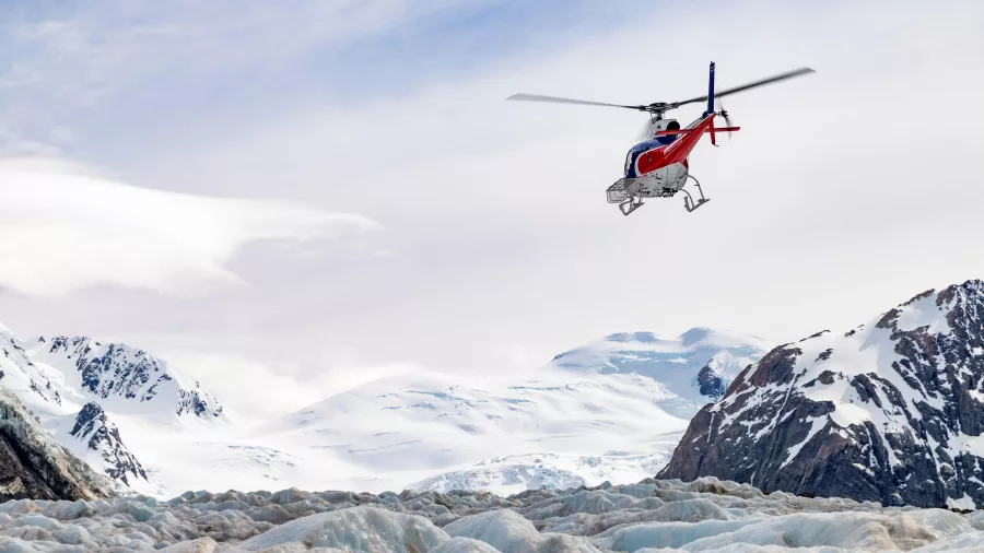 Helicopter flying above snow-covered peaks and icy terrain near Tasman Glacier
