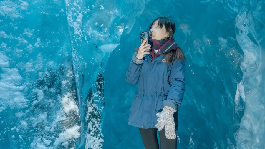 Visitor taking a photo inside a vivid blue ice cave on the Tasman Glacier