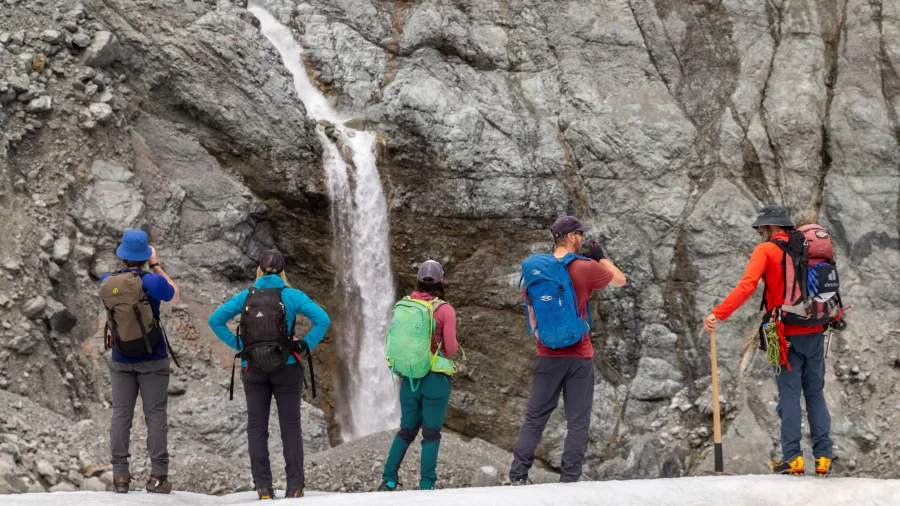 Guided group watching a powerful waterfall pouring from the glacier wall