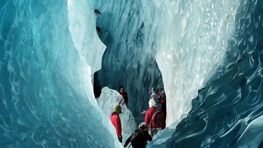 Helihikers walking through a deep ice tunnel with textured blue glacier walls