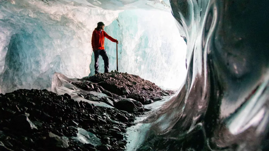 Glacier guide standing in a dark ice cave with reflective glacier walls