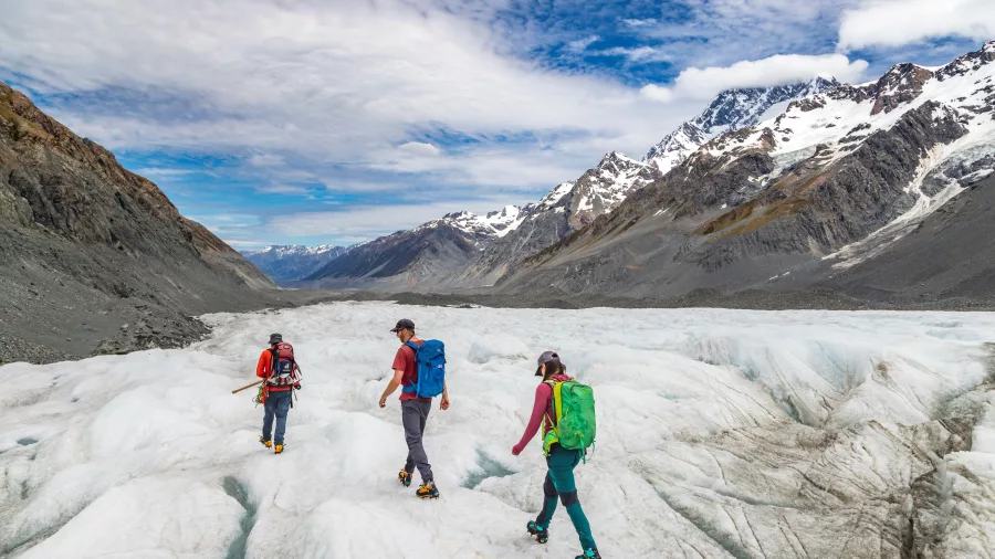 Guided group hiking across the Tasman Glacier with Mount Cook peaks in the distance