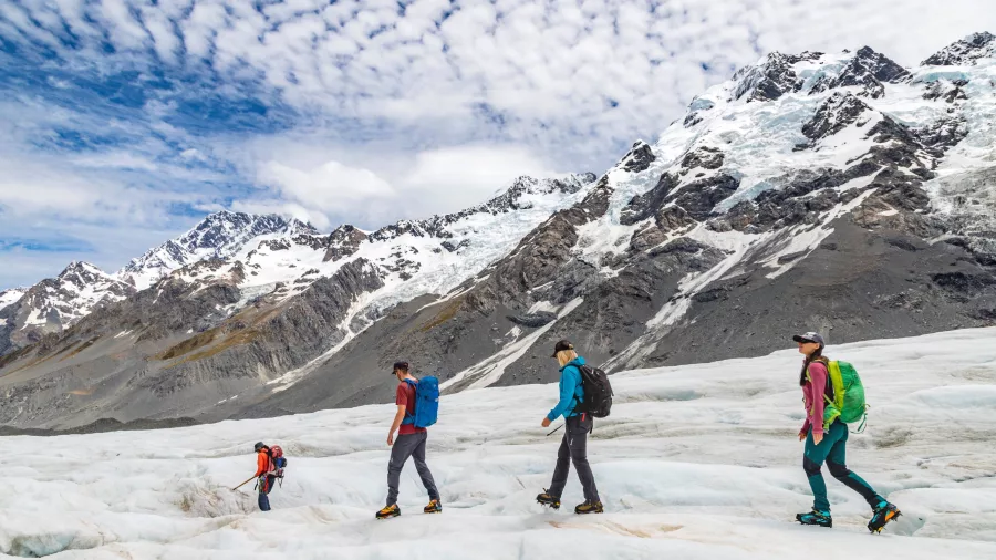 Guided group hiking across the Tasman Glacier beneath a dramatic alpine sky