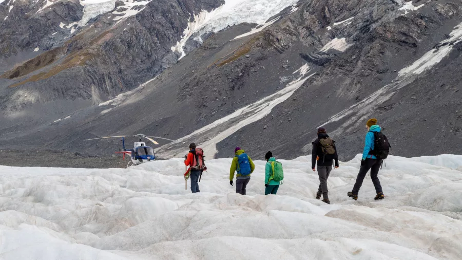 Helihikers walking across the Tasman Glacier after disembarking from helicopter