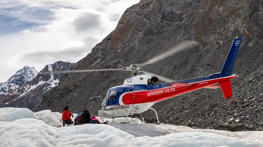Group putting on gear beside helicopter on Tasman Glacier landing site