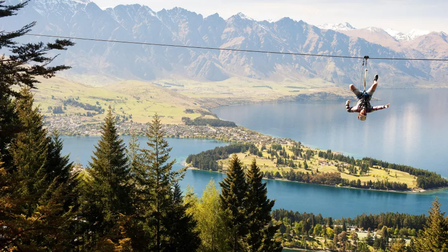 Zipliner riding upside down above Lake Whakatipu with The Remarkables in the background