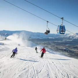 Skiers descending a groomed run under a chairlift at Coronet Peak ski field near Queenstown, New Zealand