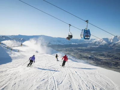 Skiers descending a groomed run under a chairlift at Coronet Peak ski field near Queenstown, New Zealand