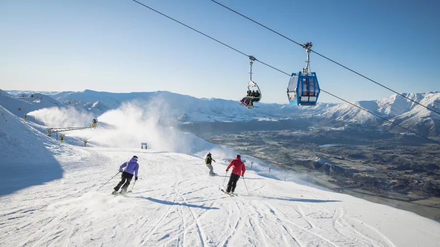 Skiers descending a groomed run under a chairlift at Coronet Peak ski field near Queenstown, New Zealand