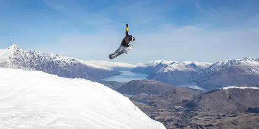 Snowboarder performing high jump trick at Coronet Peak with Queenstown and lake backdrop