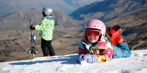 Young children enjoying the snow at Coronet Peak ski field, with alpine views over Queenstown in the background
