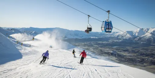 Skiers descending a groomed run under a chairlift at Coronet Peak ski field near Queenstown, New Zealand
