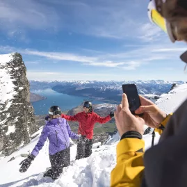 Friends posing for a photo on a snowy lookout at The Remarkables with Lake Wakatipu in the background