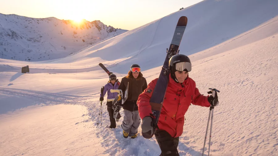 Skiers hiking uphill with gear at sunrise at The Remarkables, Queenstown