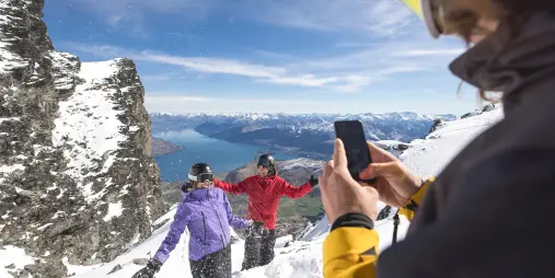 Friends posing for a photo on a snowy lookout at The Remarkables with Lake Wakatipu in the background