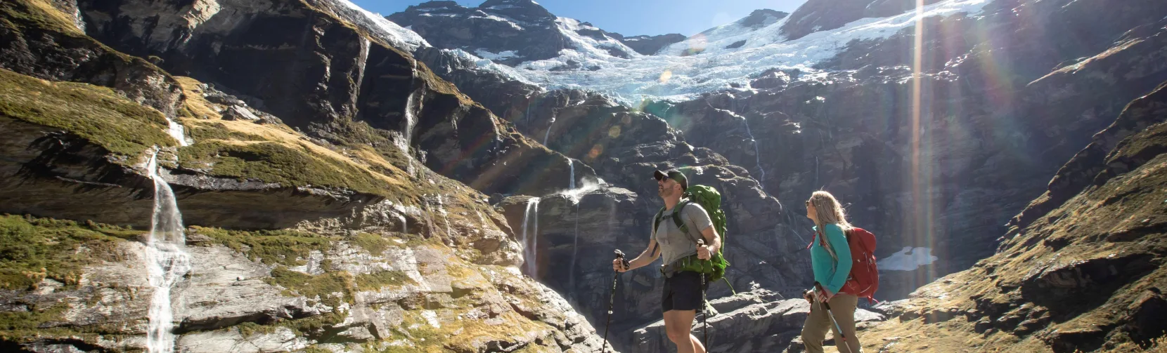 Two hikers walking toward the Earnslaw Burn glacier and waterfalls near Queenstown