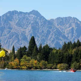 Parasailing on Lake Wakatipu with forested shoreline and The Remarkables in the background during summer in Queenstown
