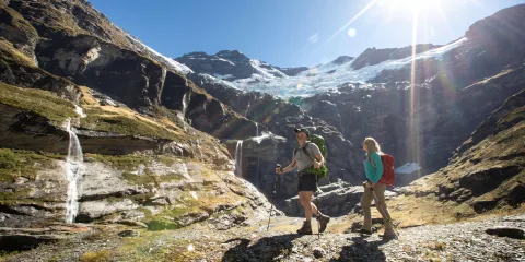 Two hikers walking toward the Earnslaw Burn glacier and waterfalls near Queenstown