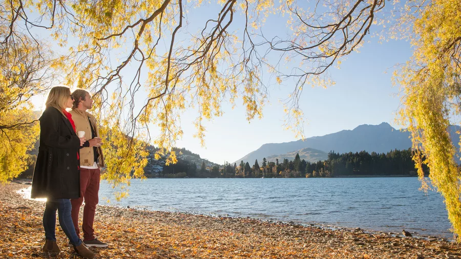 Couple walking along Queenstown Bay Beach during autumn in Otago